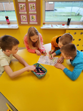 grupa przedszkolaków rysująca przy żółtym stoliku