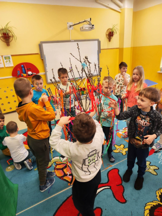 grupa przedszkolaków bawiąca się na kolorowym dywanie trzymająca kolorowe wstążki 