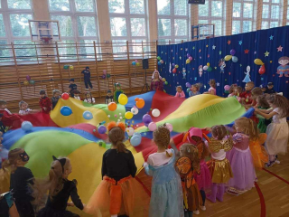 przedszkolaki w strojach bawiące się chustą animacyjną z balonami