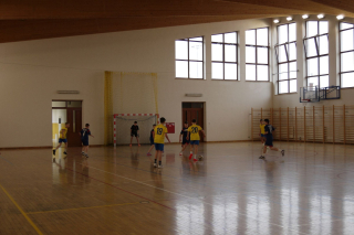 chłopcy w strojach sportowych (żółtych i niebieskich) grający w piłkę na hali sportowej