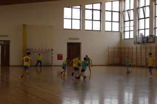 chłopcy w strojach sportowych (żółtych i niebieskich) grający w piłkę na hali sportowej