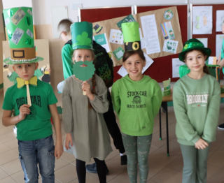 Grupa uczniów stojąca na tle jasnej ściany w sali lekcyjnej, cześć uczniów na zielono oraz w zielonych kapeluszach z okazji St. Partick
