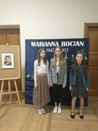 3 uczennice stojące na tle dekoracji na niebieskim tle Marianna Bocian oraz portret poetki