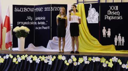 2 uczennice śpiewające na dniu papieskim, w tle dekoracja 