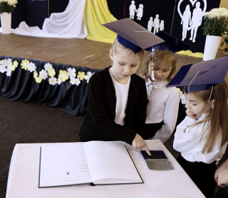 uczeń ubrany na galowo w czapce granatowej odbijający palec w księdze ślubowania 